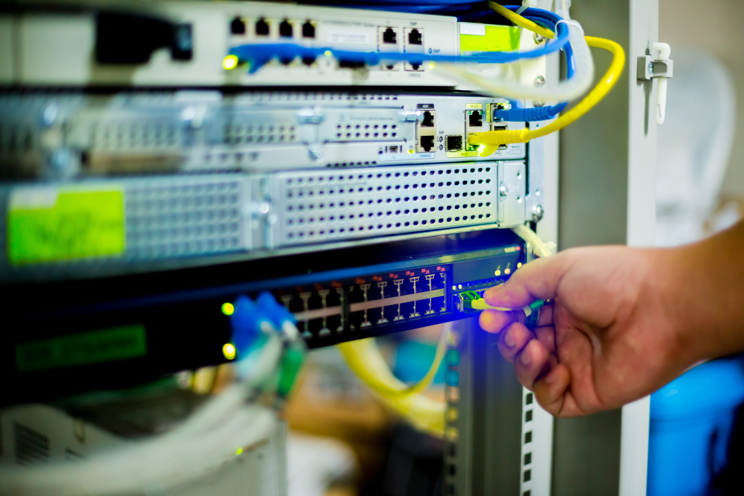 Hand holding fiber optic cord with Ethernet cables and network switching hub. Hand holding fiber optic cord with Ethernet cables and network switching hub. LAN system communication in computer control room. Fiber optic cabling.