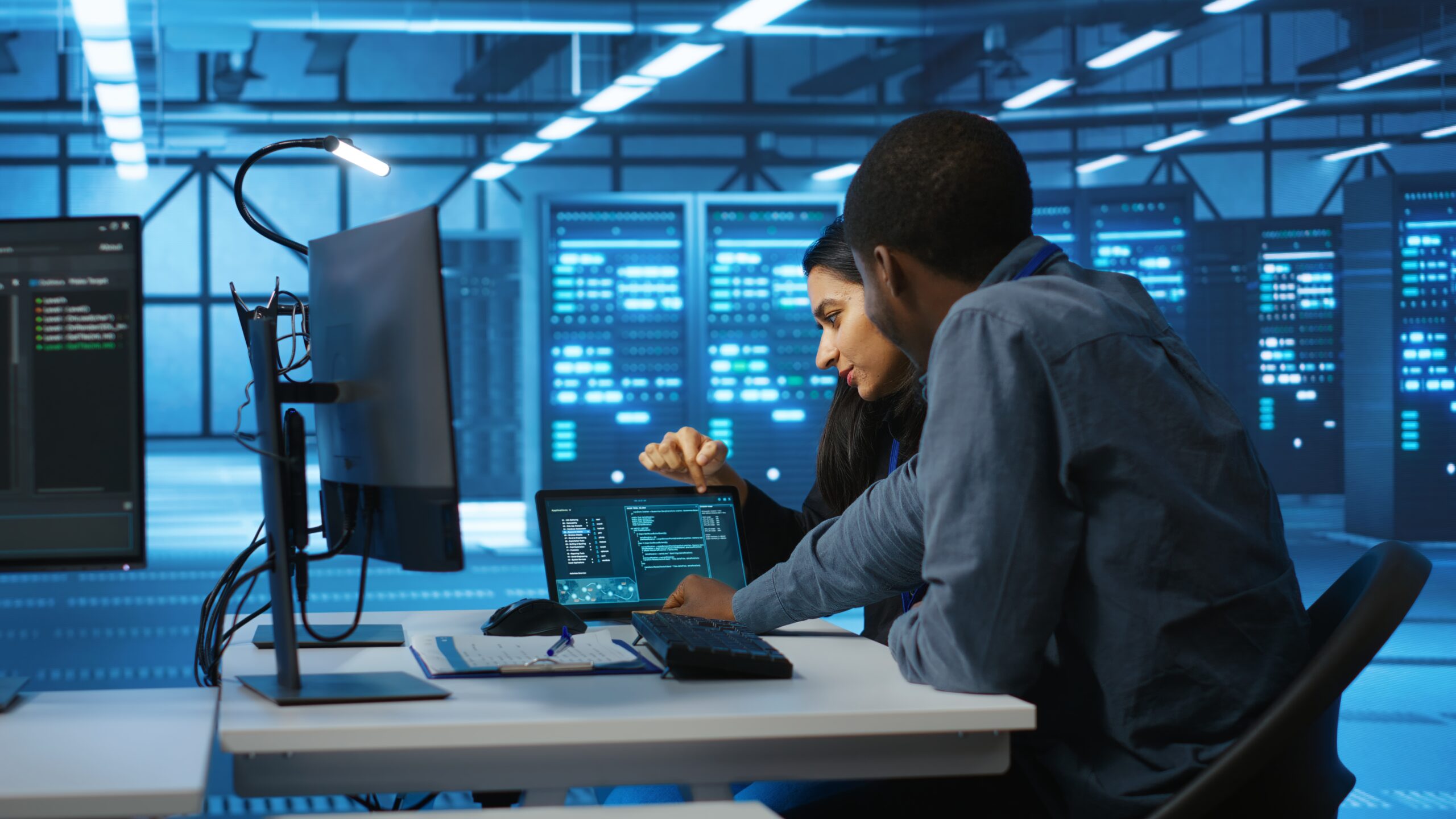 Diverse team of engineers looking at parameters in data center on tablet Multiethnic coworkers doing system analysis of server farm supercomputers using tablet. Diverse team of engineers looking at parameters in data center housing storage infrastructure